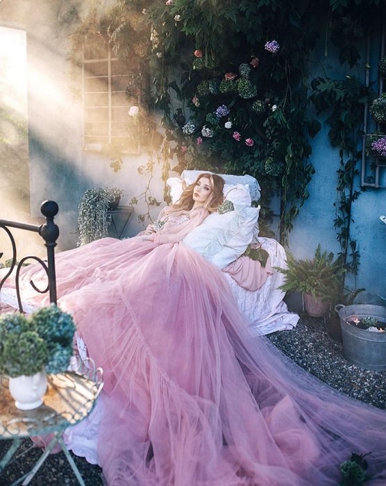 Женщина в большом розовом платье, лежащая на кровати, как пример фантазийной фотографии