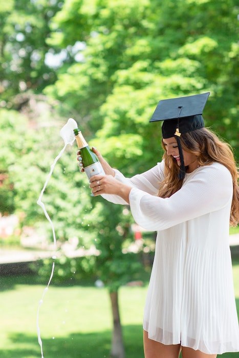 Выпускник средней школы откупоривает бутылку шампанского как классная идея для выпускного фото