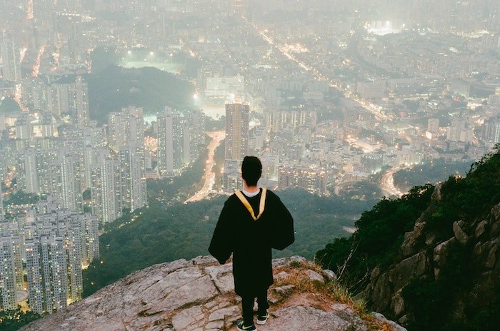 Человек в черном выпускном платье стоит и смотрит на город со скалы