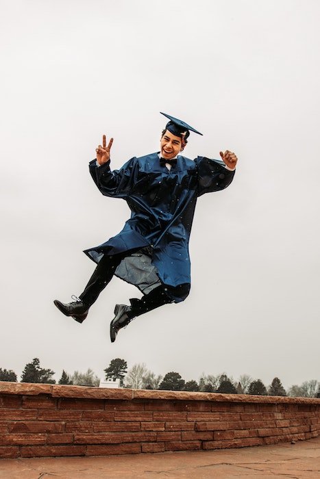 Выпускник средней школы прыгает в воздухе со знаком мира
