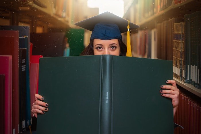 Старшеклассник листает большую книгу в шапочке выпускника для выпускной фотосессии