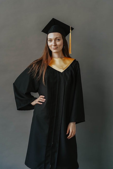 Студийный портрет выпускницы, позирующей в черной мантии и шапочке