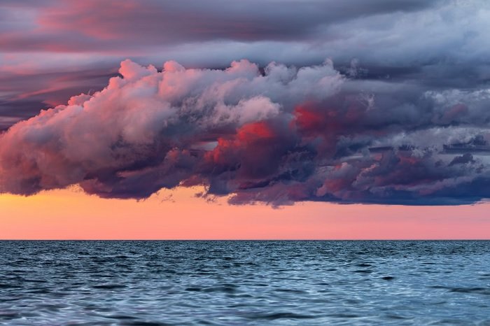 Темные облака на фоне оранжевого неба над морем моллюсков