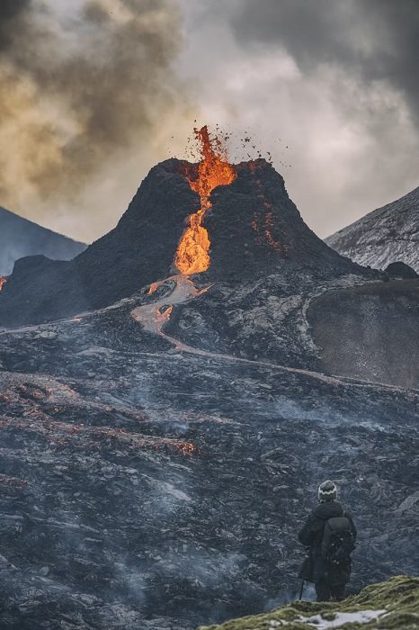Человек на переднем плане смотрит на извергающийся вулкан