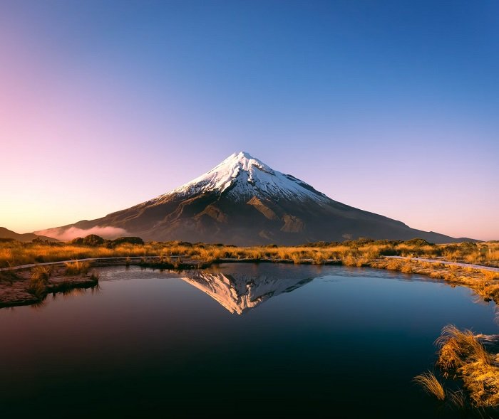 Пейзажное изображение одинокой горы, отражающейся в воде озера на переднем плане