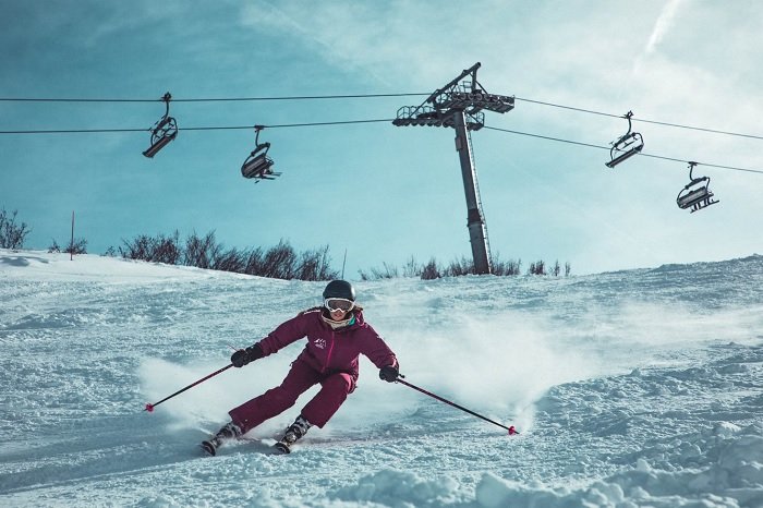 Женщина в фиолетовом лыжном костюме спускается по склону